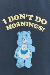 Remera azul de algodón con efecto lavado, cuello redondo y mangas cortas. Estampado frontal con un oso Care Bear y la frase "I don't do mornings!".
