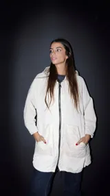 Campera color crudo combinada en pana y nylon con diseño capitoneado, corte recto, cierre frontal con cremallera, capucha y bolsillos laterales. Es de corte fino.