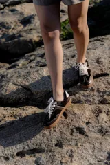 Zapatillas bajas de cuero color marrón oscuro con detalles en blanco y suela de goma color caramelo.