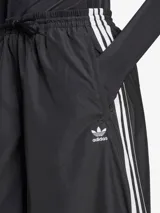 Pantalón deportivo negro de corte ancho con tres rayas blancas verticales en los laterales y logo de Adidas bordado en blanco en la parte superior de la pierna izquierda.