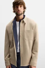Sobrecamisa negra de tejido con elasticidad, cuello solapa y manga larga acabada en puño con botón a presión. Tiene bolsillos de plastrón en el pecho y cierre frontal con botones a presión.