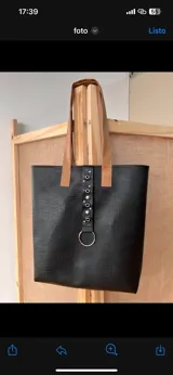 Bolso tote negro con textura símil cuero de cocodrilo, con bolsillo frontal marrón y herrajes plateados.