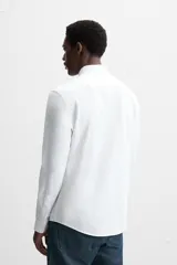 Camisa blanca de algodón, corte regular, con cuello italiano abierto, manga larga con puños abotonados y cierre frontal con botones.