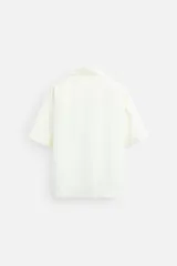 Camisa negra de corte relaxed fit, confeccionada en tejido con mezcla de modal. Tiene cuello bowling, manga corta, bolsillo de parche en el pecho y cierre frontal con botones.