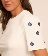 Blusa blanca de algodón con cuello redondo y mangas cortas abullonadas. Presenta pequeños bordados en color azul marino distribuidos en las mangas.