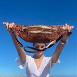 Riñonera negra con textura tipo piel de cocodrilo, con tres compartimentos con cierre y correa ajustable.