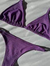 Conjunto de bikini color lila brillante, compuesto por un corpiño triangular con tirantes regulables y una bombacha colaless con tirantes regulables.
