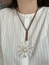 Collar con dije dorado en forma de sol y tiento de cuero marrón.
