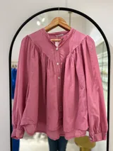Camisa rosa de manga larga con puños, cuello mao y cierre frontal con botones. Tiene corte y frunce en la parte delantera.
