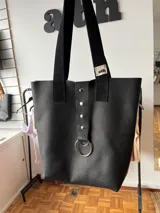 Bolso tote negro de cuero con asas cortas y largas. Presenta un bolsillo interno y cierre con dos botones.