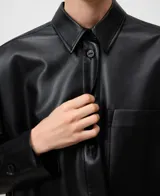 Sobrecamisa de cuero sintético color negro con cuello italiano y manga larga. Presenta cierre frontal de botones, un bolsillo de parche en el pecho, aberturas laterales y bajo redondeado con espalda ligeramente más larga.