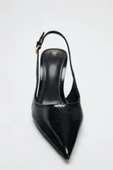 Zapato de tacón fino color negro con efecto relieve en el cuerpo, tira trasera con hebilla ajustable y acabado en punta.