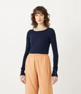 Suéter de punto acanalado color azul marino, con cuello barco y mangas largas con botones decorativos en los puños.