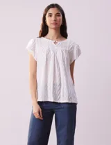 Blusa blanca labrada con cuello a la base, escote en V y aplique metálico. Tiene mangas cortas superpuestas.
