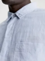 Camisa celeste de lino y algodón, de corte regular, manga larga, cuello en punta, cierre de botones oculto y bolsillo de parche en el pecho con monograma de Calvin Klein en la misma gama de tonos.