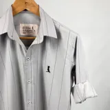 Camisa de vestir de algodón color gris claro con finas rayas verticales negras, cuello italiano, manga larga con puños abotonados y logo bordado en el pecho. Marca Duxon Originals.