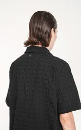 Camisa negra de manga corta con textura y cuello clásico.