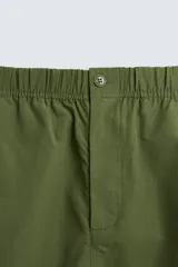 Bermuda color verde militar, relaxed fit, confeccionada en tejido técnico ligero. Cintura elástica ajustable con cordón interior, pliegues frontales, bolsillos delanteros y traseros con solapa, bolsillos cargo con solapa en perneras. Cierre frontal con cremallera y botón.