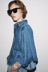 Camisa de denim azul con cuello solapa y mangas amplias tipo kimono. Tiene efecto lavado y cierre frontal con botones ocultos.