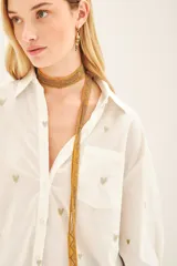 Camisa blanca de algodón con bordado de corazones dorados, corte amplio, cuello clásico, cartera con botones ocultos y bolsillo en el pecho.