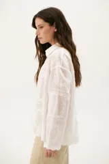 Camisa blanca con bordado floral, de corte holgado y manga larga.