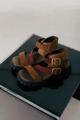 Sandalias de cuero marrón con tiras cruzadas y hebillas doradas.