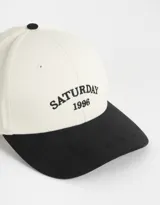 Gorra de béisbol bicolor, con cuerpo de canvas color crema y visera de gamuza color marrón. Tiene bordado frontal con la palabra "Wednesday" y el número "1996".