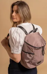 Mochila urbana de diseño compacto, color violeta/malva, con acabado ligeramente brillante. Presenta un compartimento principal con doble cierre superior y bolsillos laterales con cierre.