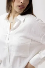 Camisa blanca de lino, de corte holgado, con cuello clásico, cierre frontal con botones, bolsillo en el pecho y mangas largas con puños abotonados.