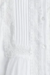 Blusa blanca de algodón con cuello mao, pechera con jaretas e inserciones de encaje, botones frontales, canesú fruncido en la espalda y mangas largas abullonadas con pinzas y abertura con botón en los puños.