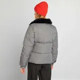 Campera puffer gris de franela con cuello de piel sintética negra, cierre frontal con cremallera dorada y bolsillos laterales.