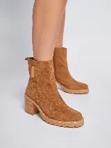 Bota corta de gamuza color marrón, con taco cuadrado de madera y suela track. Presenta un tirador en la parte posterior. Confeccionada 100% en cuero genuino.