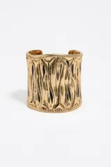 Pulsera brazalete rígido de metal dorado con diseño de líneas verticales en relieve y detalles de esmalte negro.