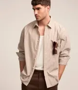 Camisa masculina de tricolina con rayas verticales, corte relaxed, cuello tradicional, mangas largas, bolsillo en el pecho y cierre abotonado.