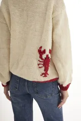 Sweater tejido a mano en Uruguay, de lana merino color crudo con cuello y dibujo de langosta en rojo.
