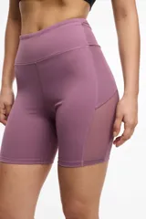 Calza deportiva corta color lila, de cintura alta, con bolsillos laterales y transparencias de microtul en los laterales.