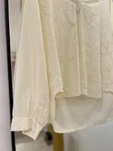 Blusa color crudo con bordados calados, cuello camisero y mangas largas con puño.