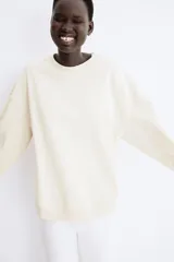 Buzo de tejido liso color crema, con cuello redondo acanalado, hombros caídos y puños y bajo acanalados.