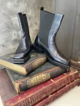 Bota de cuero negra de caña media con elásticos laterales en la caña y punta cuadrada.
