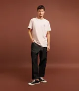 Remera de algodón color rosa claro, de corte clásico, con cuello redondo y manga corta. Presenta un pequeño estampado de un timón en el pecho y un estampado con letras en la espalda.