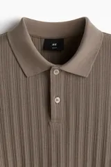 Remera polo marrón en punto texturizado de peso medio, de manga corta con cuello, tapeta de botones y bajo recto. Corte ajustado que realza el contorno del cuerpo creando una silueta entallada.