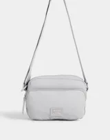 Bandolera gris claro de tela deportiva con bolsillo frontal, correa larga regulable, acceso con cierre superior y tag de goma.