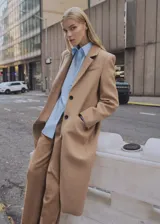 Abrigo largo color camel, con cuello de solapa, doble botonadura y bolsillos laterales con solapa. Confeccionado en mezcla de lana con forro interior.