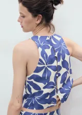 Top crop sin mangas con cuello redondo y diseño recto. Presenta un estampado floral en tonos azules sobre fondo crema, tirantes anchos y cierre de botones en la parte posterior. Confeccionado en una mezcla de viscosa y lino con forro de algodón.