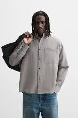 Camisa de hombre relaxed fit con cuello solapa, manga larga con puño abotonado, bolsillo de parche en el pecho y cierre frontal con botones. Diseño a cuadros en tonos gris y blanco.