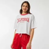 Camiseta corta blanca con cuello redondo y ribete rojo. Estampado frontal con la palabra "California" en rojo y debajo "Santa Mónica".