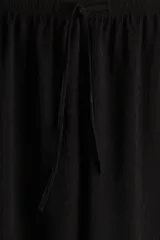 Pantalón negro de punto con textura, corte holgado, tiro alto, piernas rectas, elástico revestido en la cintura y cordón para ajustar.