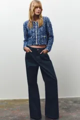 Chaqueta corta azul con tejido de punto entrelazado, cuello redondo, manga larga, bolsillos delanteros de plastrón y cierre frontal con botones dorados.