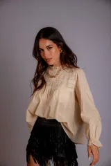 Camisa color crema con cuello alto y mangas largas con volados en los puños. Presenta detalles de crochet y broderie en el frente.