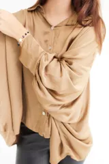 Camisa color beige de satén con corte holgado, cuello camisero y mangas largas con puños abotonados.